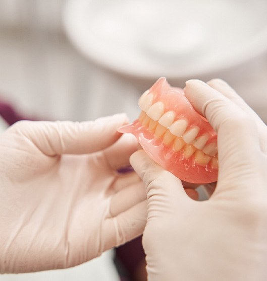 White-gloved hands holding complete set of dentures