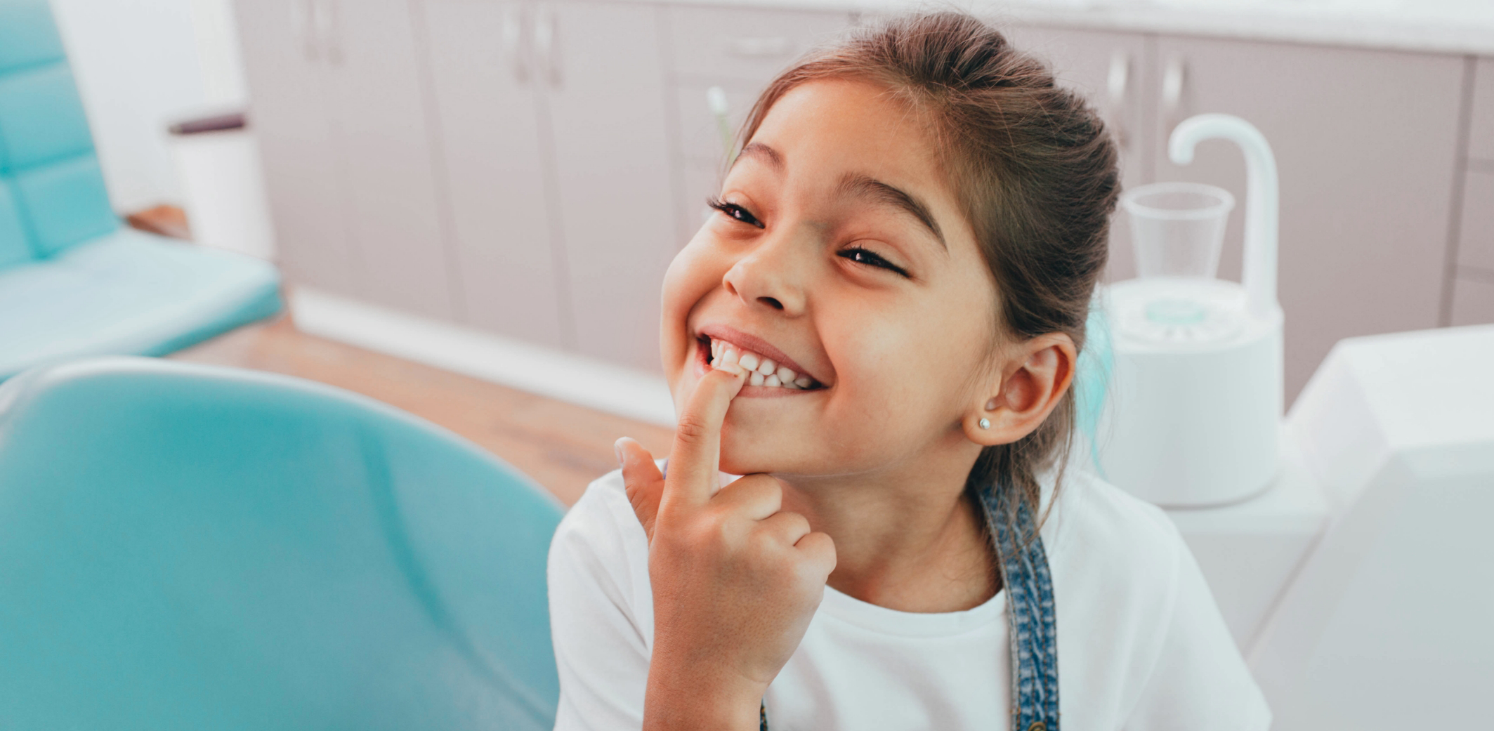 Little girl pointing to smile in chair while visiting childrens dentist in Rowlett